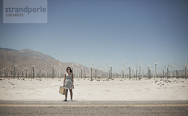Eine junge Frau mit einem Koffer steht am Rand der Autobahn.