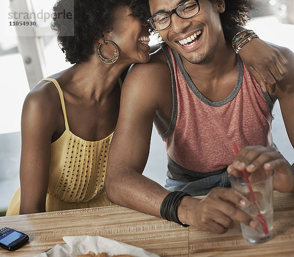 Ein junges Paar sitzt zusammen  umarmt sich und lacht in einem Diner.