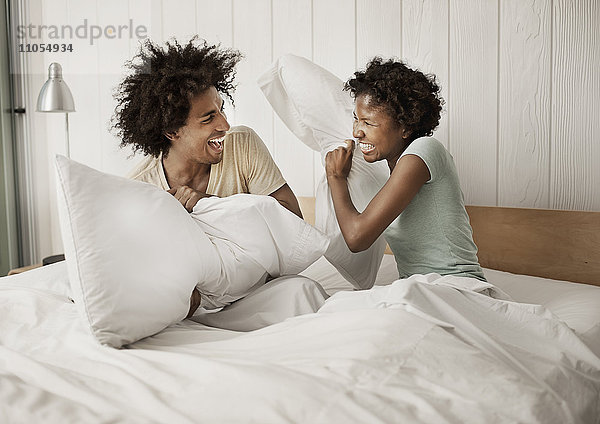 Ein junges Paar sitzt im Bett und streitet mit Kissen.