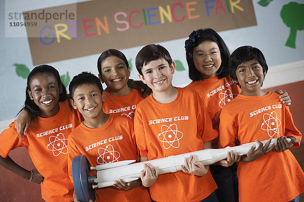 Studenten im Wissenschaftsclub stehen unter dem Zeichen Green Science Fair und halten eine lange Rakete in der Hand.