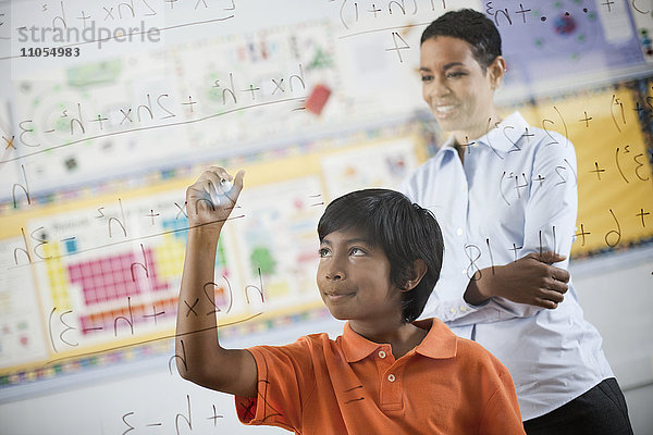 Ein Schüler schreibt mit Stiften Formeln und Gleichungen auf eine durchsichtige Plexiglastafel.