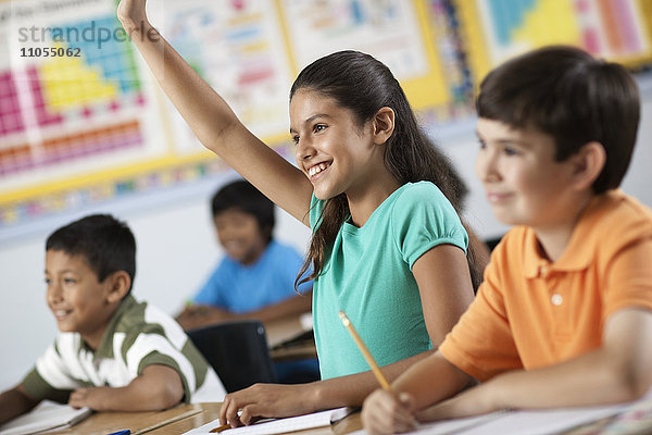 Eine Gruppe junger Mädchen und Jungen in einem Klassenzimmer  Klassenkameraden. Ein Mädchen hebt ihre Hand.