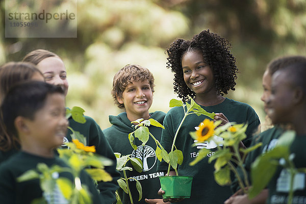 Kinder in einer Gruppe lernen etwas über Pflanzen und Blumen  tragen Pflanzen und Sonnenblumen.