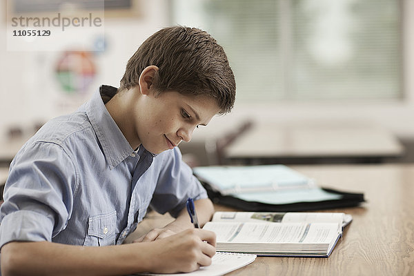 Ein Junge sitzt in der Klasse am Schreibtisch  benutzt Schulbücher und hält einen Stift.
