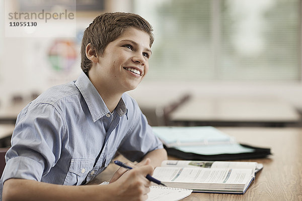 Ein Junge sitzt in der Klasse am Schreibtisch  benutzt Schulbücher und hält einen Stift.