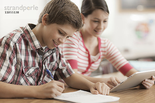 Zwei Kinder  ein Junge und ein Mädchen  sitzen in der Klasse und teilen sich ein digitales Tablett.