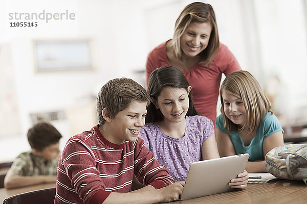 Eine Gruppe von Schülern im Unterricht und ein erwachsener Lehrer betrachten ein digitales Tablett.