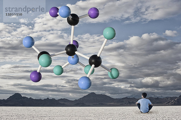 Ein Junge sitzt auf dem Boden in einem offenen Raum im Wüstengebiet  neben einer großen Molekularstruktur.