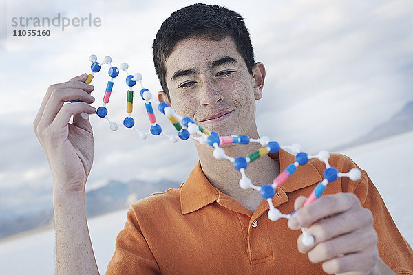 Ein Teenager in einem orangefarbenen Polohemd hält ein Molekularstrukturmodell und untersucht es.
