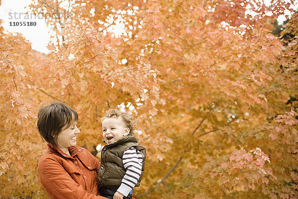 Eine Frau  die ein Kind im Freien hält  umgeben von Bäumen in Herbstfarben.