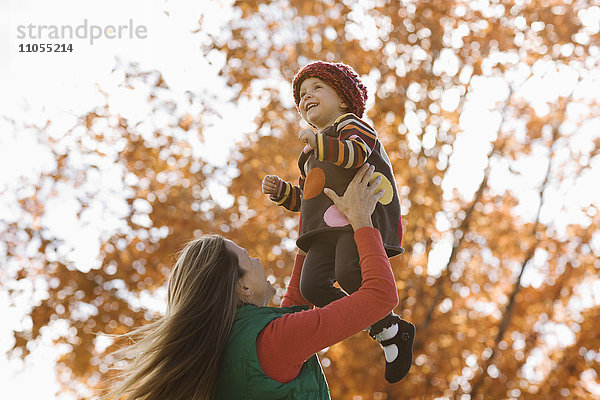 Eine Frau hebt ein Kind in die Luft  eine Mutter und ihre Tochter im Herbst im Freien