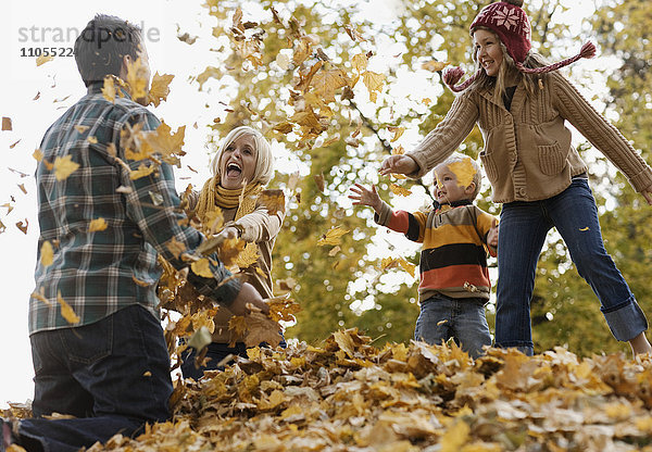 Eine Familie  Erwachsene und zwei Kinder spielen im Herbstlaub.