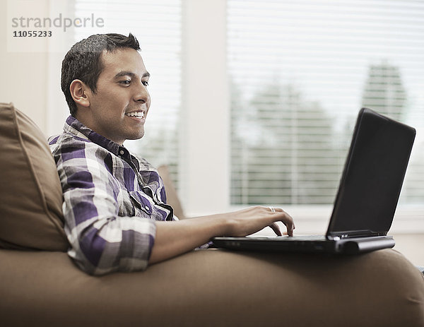 Ein Mann sitzt auf einem Sofa und benutzt einen Laptop-Computer.
