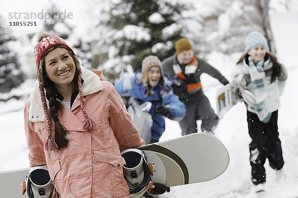 Schnee im Winter. Ein Mädchen  das ein Snowboard trägt  und drei Kinder  die hinter ihr herlaufen.