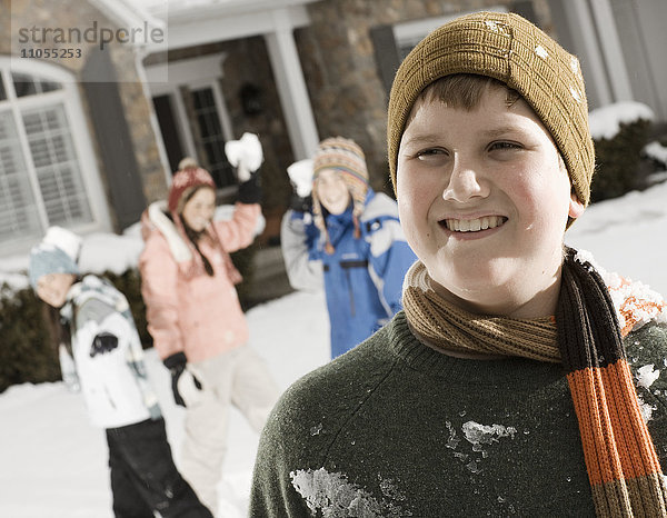 Schnee im Winter. Ein Junge im Vordergrund und drei Kinder hinter ihm  die sich darauf vorbereiten  Schneebälle zu werfen.