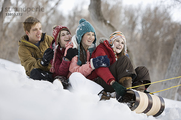 Vier junge Leute auf einem großen Schlitten  die bergab über den Schnee rutschen.