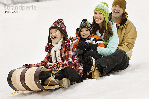 Eine Familie mit zwei Erwachsenen und zwei Kindern sitzt auf Schlitten auf dem Schnee.
