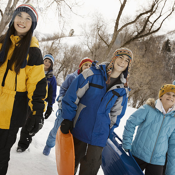 Eine Gruppe von Kindern  Jungen und Mädchen  die Schlitten über den Schnee tragen.