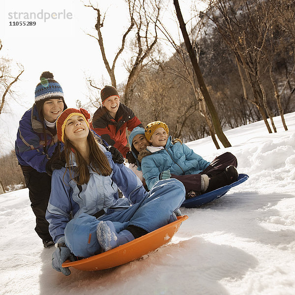 Eine Gruppe von Kindern  Jungen und Mädchen  die auf Schlitten auf dem Schnee fahren.