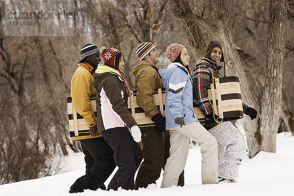 Fünf junge Leute tragen einen Holzschlitten über den Schnee.