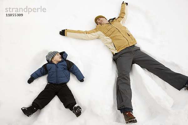 Zwei Menschen  ein Mann und ein Kind  die im Schnee liegen  bilden Schnee-Engelformen.