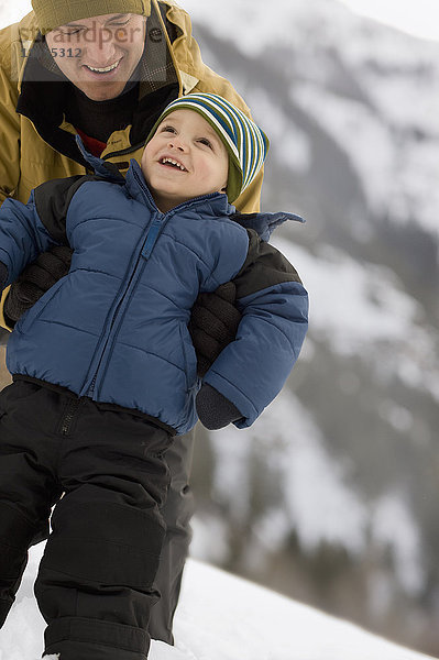Ein Mann mit einem kleinen Kind  eingehüllt gegen die Kälte  in den Bergen im Schnee.
