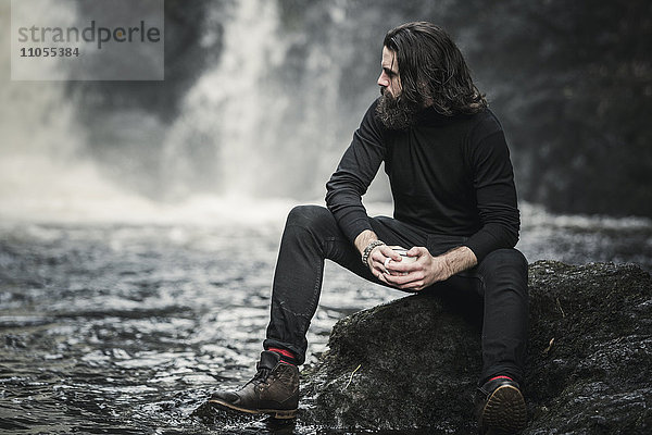 Ein Mann sitzt an einem schnell fließenden Wasserstrom über Felsen.