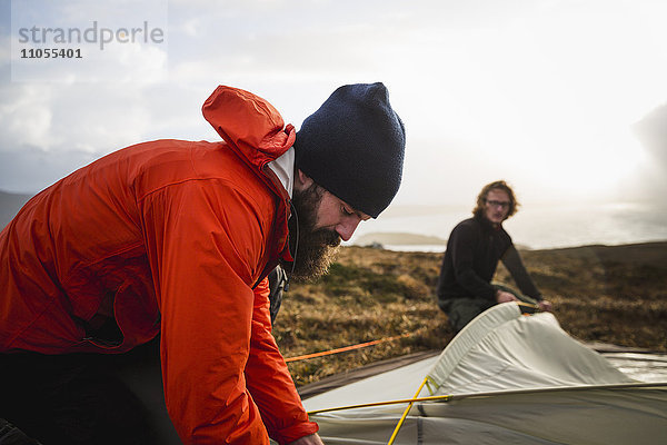 Zwei Männer  die ein kleines Zelt auf offenem Gelände halten und aufstellen. Wildes Zelten.
