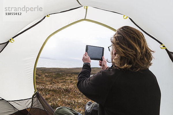 Ein Mann sitzt im Schutz eines Zeltes und schaut hinaus  fotografiert mit einem digitalen Tablett