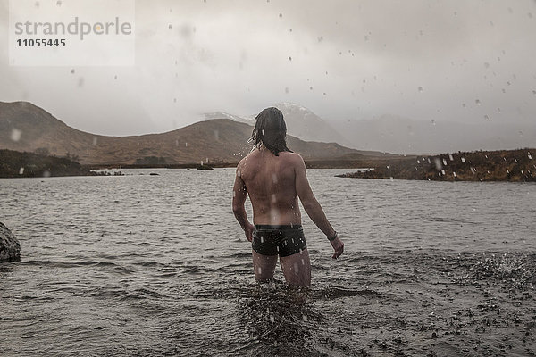 Ein Mann  der in Badehose mit den Oberschenkeln tief im Meerwasser steht.