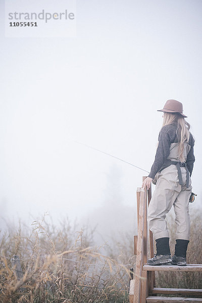 Eine Frau  die auf einem Holzstil im Nebel steht.