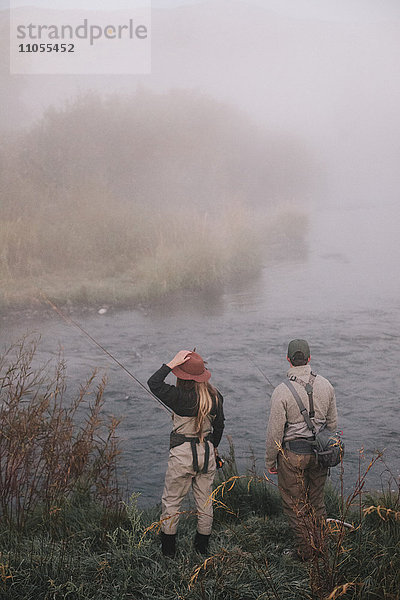 Zwei Menschen  Mann und Frau  stehen am Flussufer und schauen über das Wasser.