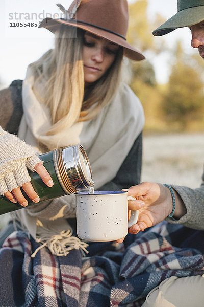 Eine Frau gießt bei einem Winterpicknick ein heißes Getränk aus einer Vakuumflasche in einen Becher.