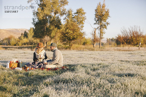 Ein Paar  ein Mann und eine Frau beim Winterpicknick  auf einem Schottenkaro-Teppich sitzend.