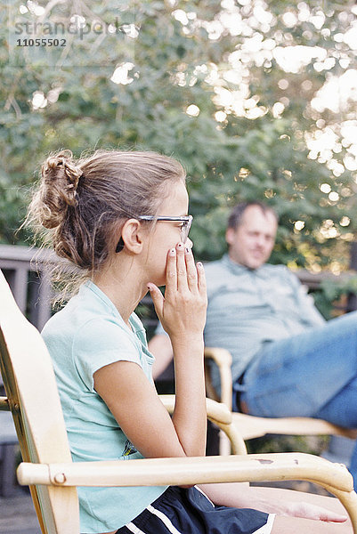 Ein reifer Mann und ein junges Mädchen sitzen in einem Garten.