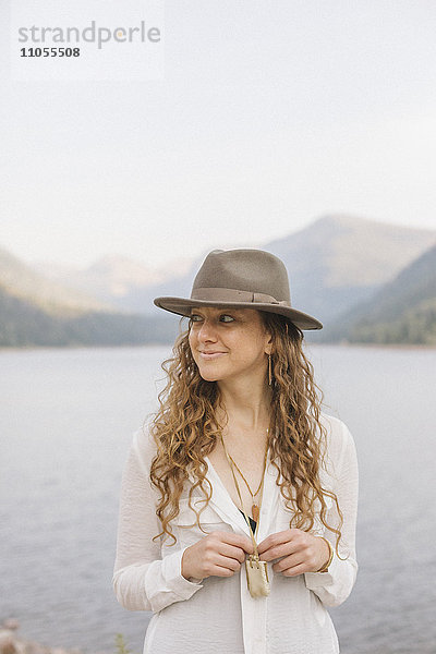 Eine Frau mit breitkrempigem Hut an einem Bergsee.