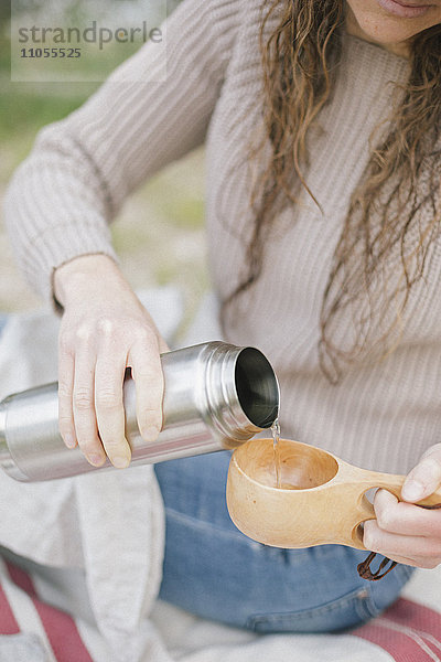 Eine Frau gießt ein Getränk aus einer Flasche in einen Becher.