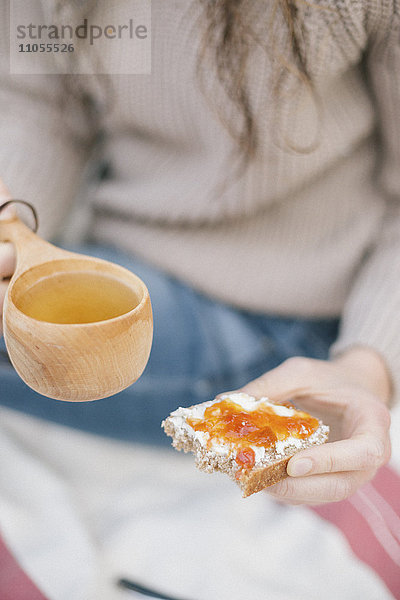 Eine Frau hält eine Tasse Tee und eine Scheibe Brot und Marmelade in der Hand.