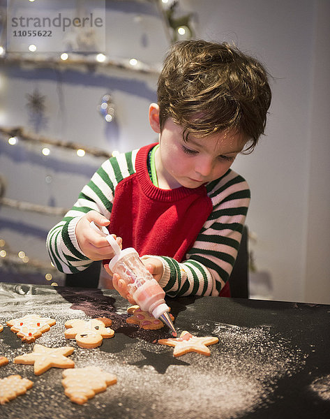 Ein Junge in einer roten Schürze schmückt Weihnachtsplätzchen mit einer Vereisungspistole.