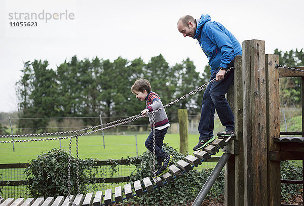 Ein Junge und sein Vater auf einem Klettergerüst  auf einem Gang balancierend.