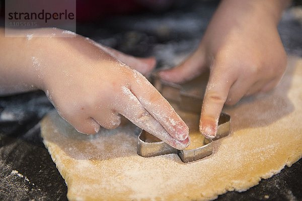 Ein Kind  das eine Ausstechform benutzt  um Weihnachtsplätzchen zu backen.