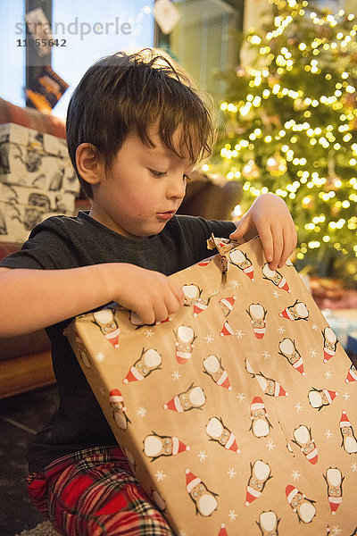 Eine Familie zu Hause am Weihnachtstag. Ein Junge packt ein großes Geschenk aus.