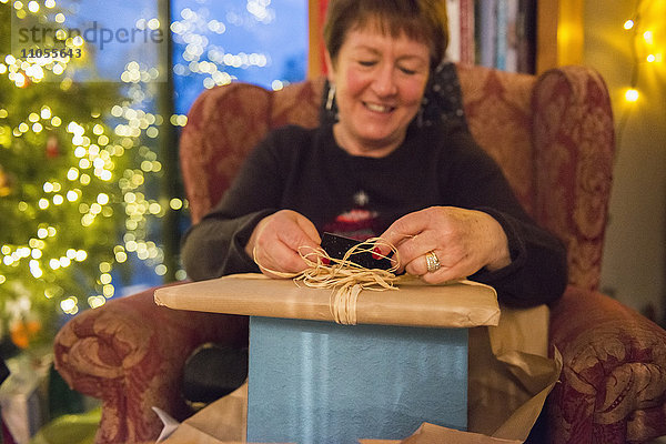 Eine Familie zu Hause am Weihnachtstag. Eine reife Frau  die einen Stapel Geschenke öffnet.
