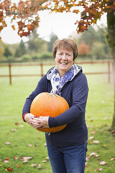 Eine Frau im Freien  die einen großen orangefarbenen Kürbis hält.