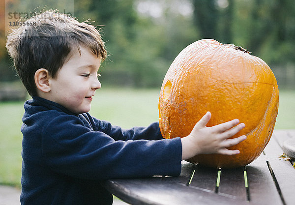 Ein kleiner Junge hält einen großen orangenhäutigen Kürbis in der Hand.