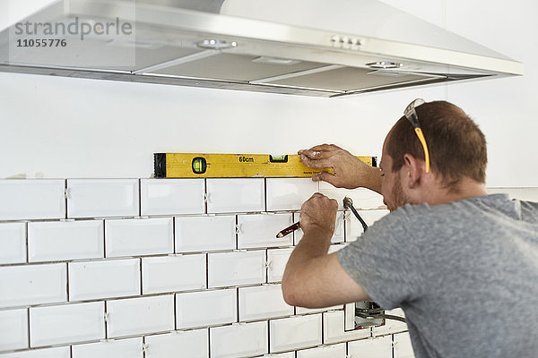 Ein Mann  der in einer neuen Küche arbeitet  ein Fliesenleger  der Fliesen an der Wand hinter dem Herd anbringt.