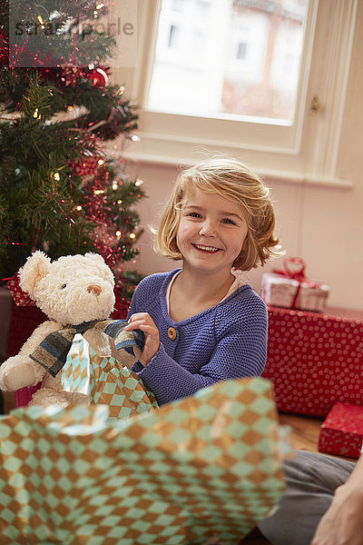 Ein Mädchen packt am Weihnachtstag ein Plüschtier  einen Teddybär  aus.