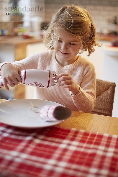 Ein Mädchen  das an einem Tisch einen Weihnachts-Cracker öffnet.