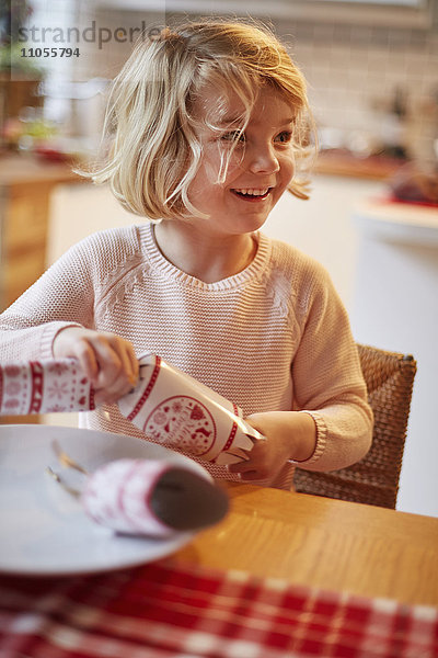 Ein Mädchen  das an einem Tisch einen Weihnachts-Cracker öffnet.