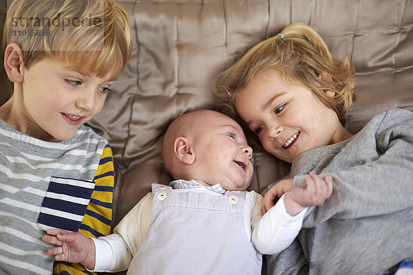 Drei Kinder liegen auf einem Bett  ein Junge und ein Mädchen mit einem Baby dazwischen.